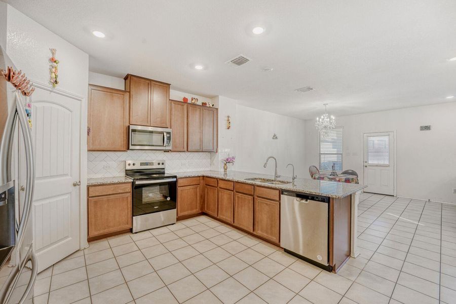 Kitchen with stainless steel appliances, light stone countertops, a peninsula, decorative backsplash, and hanging light fixtures