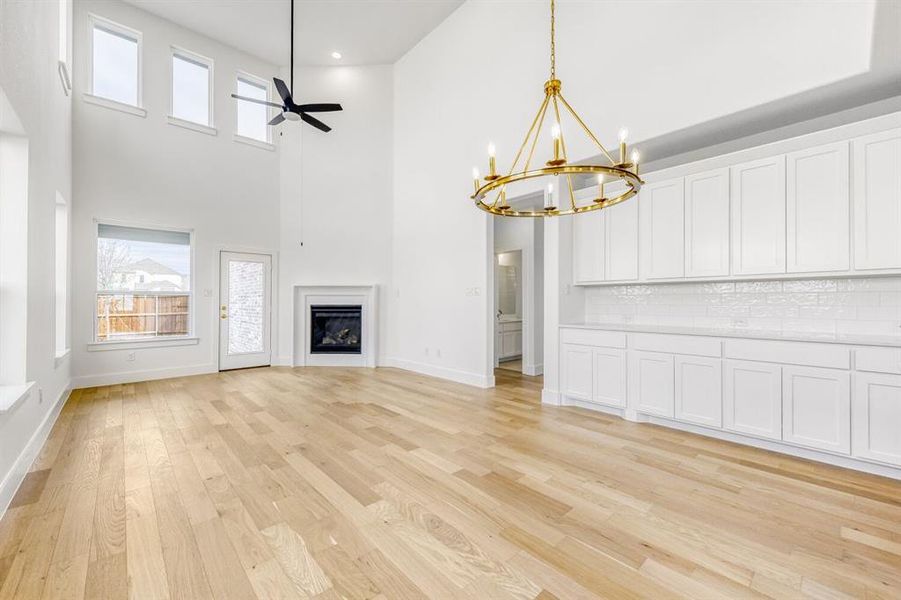 Unfurnished living room with ceiling fan, a high ceiling, suspended lighting, a fireplace, and light wood-type flooring