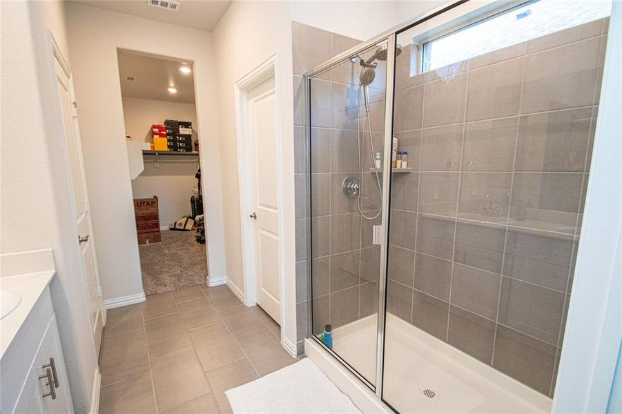 Bathroom featuring vanity, a stall shower, light tile patterned floors, and a spacious closet Bathroom featuring vanity, a stall shower, light tile patterned floors, and a spacious closet