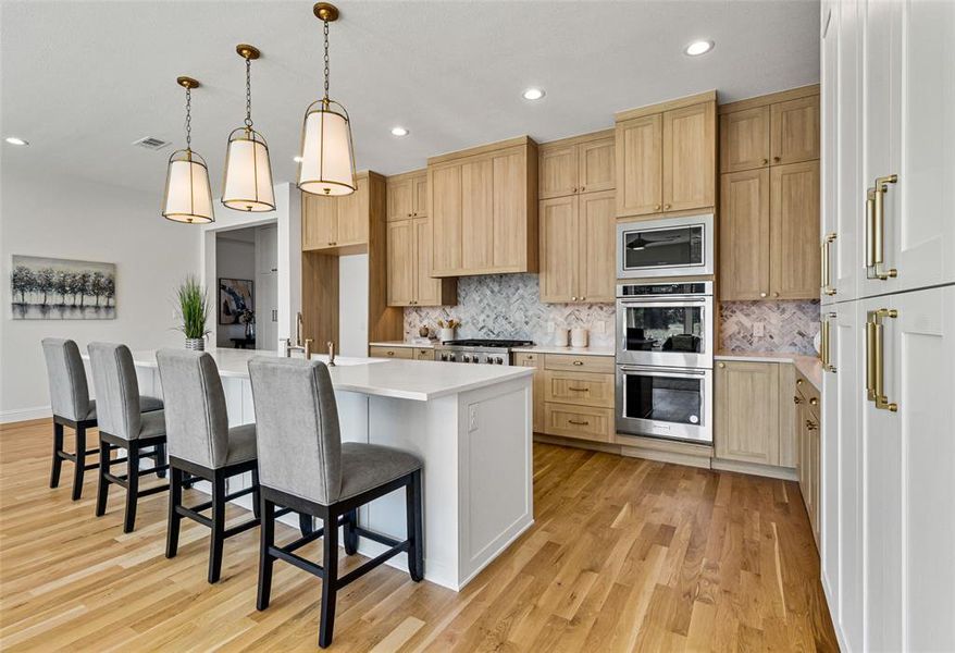 Kitchen with a breakfast bar area, hanging light fixtures, a center island with sink, appliances with stainless steel finishes, and light hardwood / wood-style floors