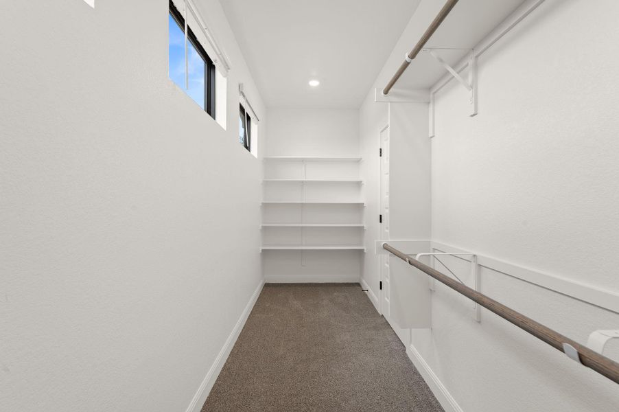Large walk in primary closet with built-in shelves and windows allowing natural light