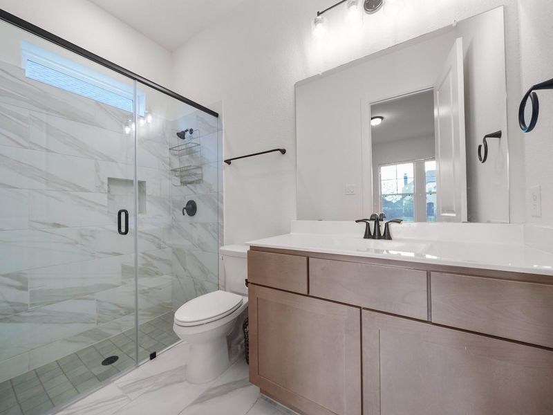 This ensuite bath is finished with modern fixtures, a sleek vanity, and a walk-in shower, ensuring convenience and comfort for guests or family members who need their own private space.
