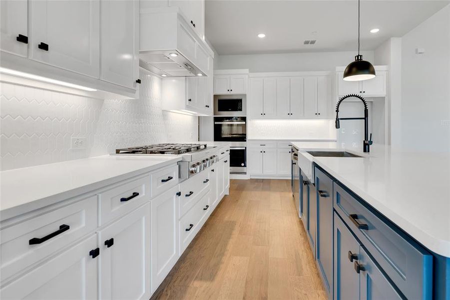 Kitchen with light wood-type flooring, white cabinets, pendant lighting, tasteful backsplash, and blue cabinets