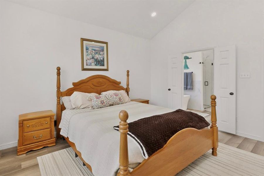 Vaulted ceiling with recessed lighting, wood-finish flooring, white walls, and a visible bathroom entrance