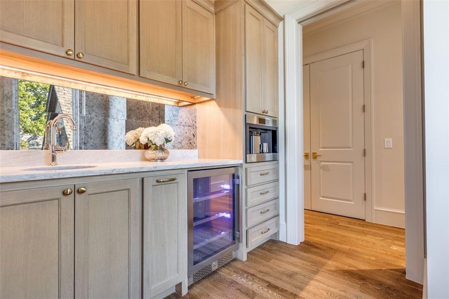 Kitchen with wine cooler, light wood finished floors, light stone counters, stainless steel microwave, and tasteful backsplash Kitchen with wine cooler, light wood finished floors, light stone counters, stainless steel microwave, and tasteful backsplash