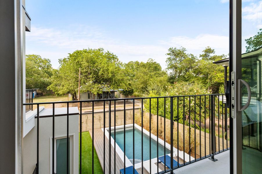 A private upper-level balcony overlooks a sparkling in-ground pool surrounded by lush green trees. A private upper-level balcony overlooks a sparkling in-ground pool surrounded by lush green trees.