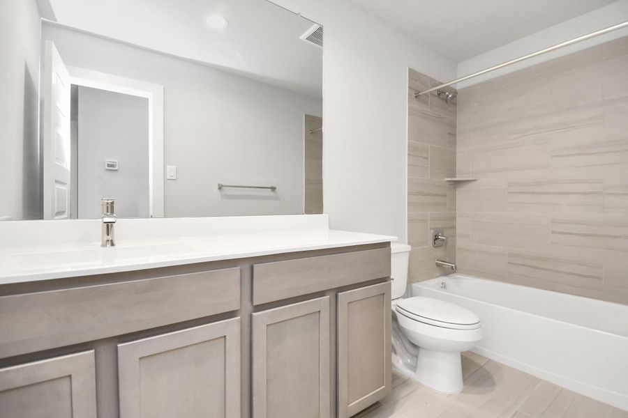Indulge in refined charm in the secondary bathroom, where the tile flooring harmonizes with a bath/shower combo surrounded by tasteful tile. Light wood cabinets, coupled with a gorgeous countertop, elevate the space, cultivating a truly welcoming atmosphere. Sample photo of completed home with similar floor plan. Actual colors and selections may vary.