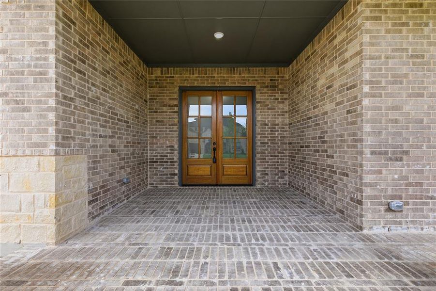 Covered entryway featuring a double wood-paneled door with glass inserts, brick-patterned flooring, and a recessed ceiling light fixture Covered entryway featuring a double wood-paneled door with glass inserts, brick-patterned flooring, and a recessed ceiling light fixture