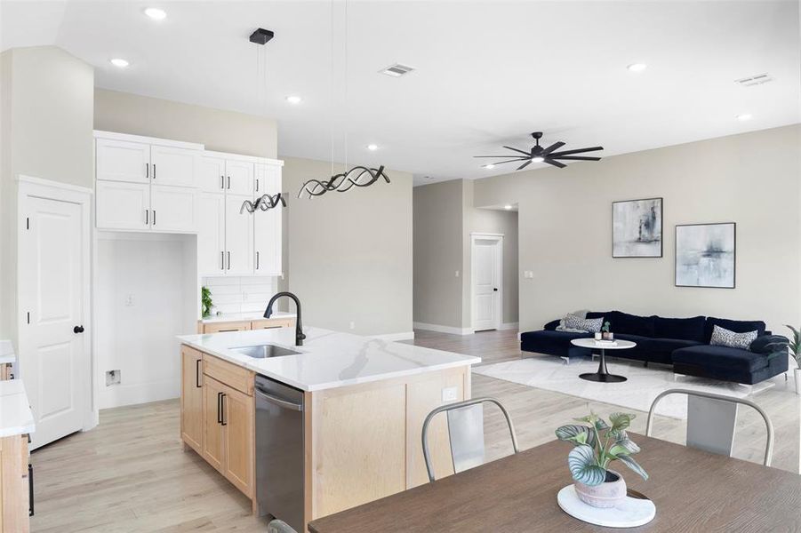 Kitchen featuring a center island with sink, sink, hanging light fixtures, stainless steel dishwasher, and light hardwood / wood-style flooring