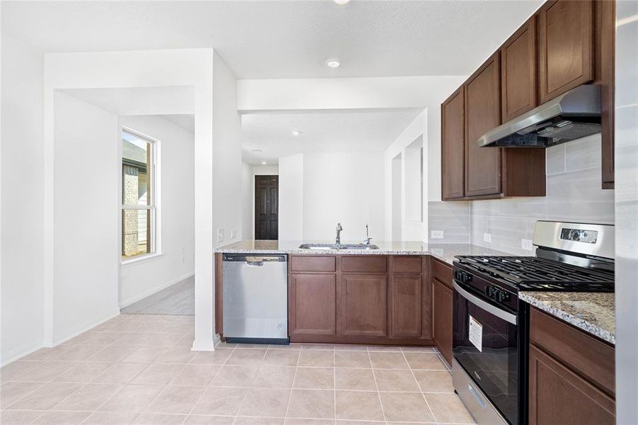 This spacious kitchen features high ceilings, stained wood cabinets, granite countertops, SS appliances, modern tile backsplash, recessed lighting, and a walk-in pantry all overlooking your huge family room.