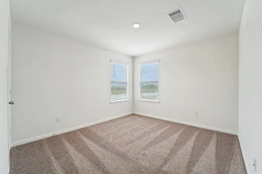 This secondary bedroom offers comfort and style with plush carpeting, neutral paint tones, recessed lighting, large windows with blinds, and a walk-in closet.