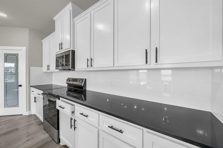 Kitchen with white cabinetry, tasteful backsplash, light wood-type flooring, and stainless steel appliances