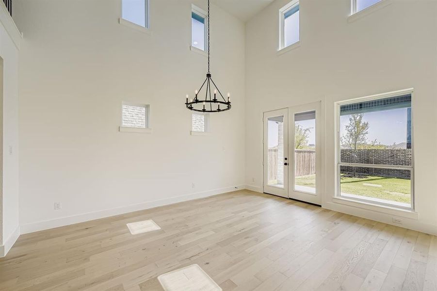 Unfurnished dining area with a chandelier, light wood-type flooring, french doors, and a towering ceiling Unfurnished dining area with a chandelier, light wood-type flooring, french doors, and a towering ceiling