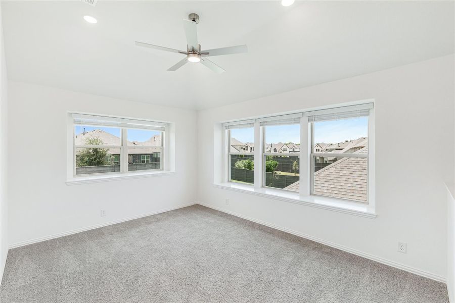Empty bedroom with gray carpet, ceiling fan, and three large windows overlooking neighboring homes Empty bedroom with gray carpet, ceiling fan, and three large windows overlooking neighboring homes