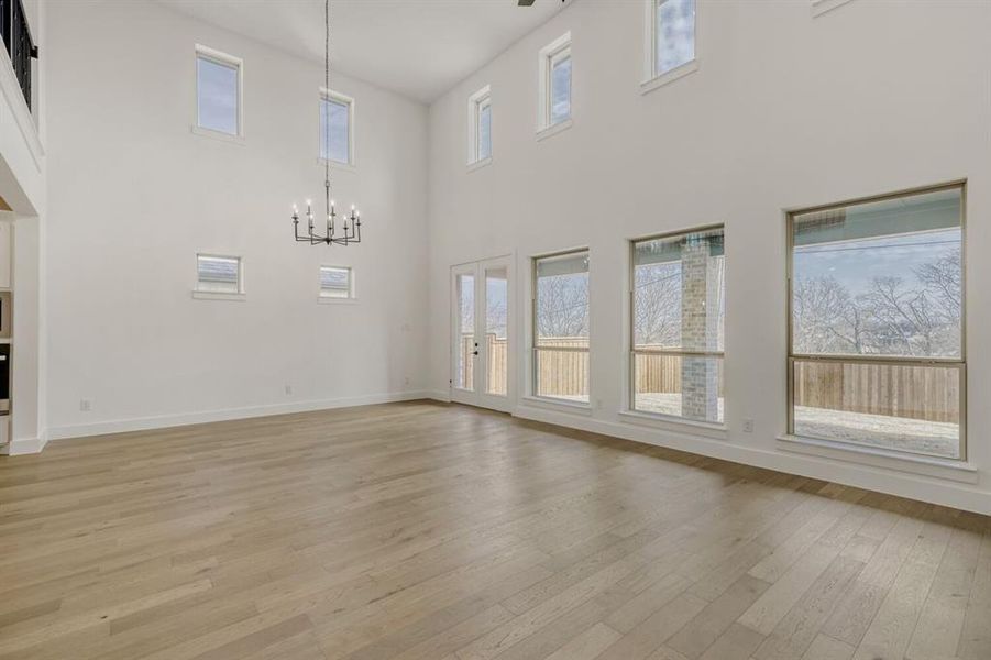 Unfurnished living room featuring light wood-style flooring, hanging lights, and a high ceiling