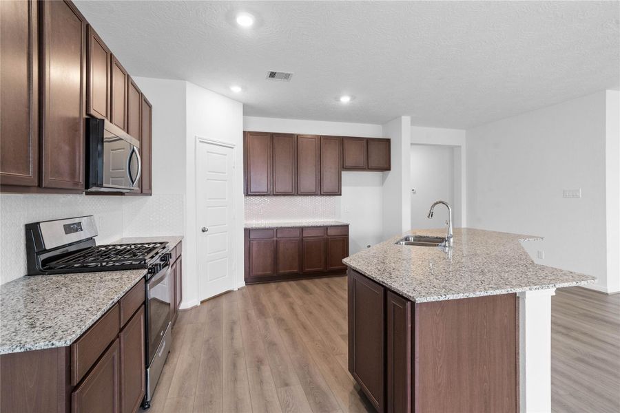 A true chef’s dream, this spacious and open kitchen boasts high ceilings, recessed lighting, rich stained wood cabinets, granite countertops, stainless steel appliances, a modern tile backsplash, extended counter space, an island, and a walk-in pantry—all with a clear view of the spacious Great Room.