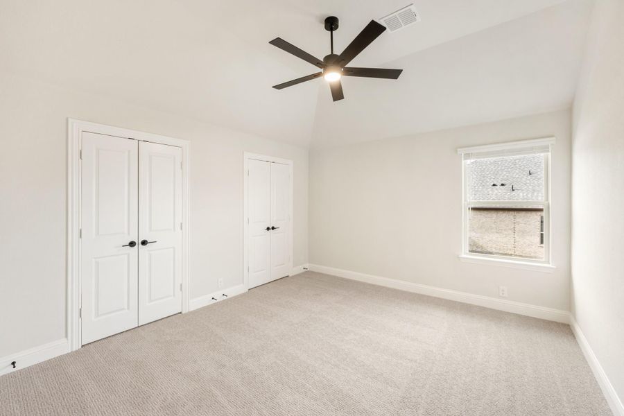 Empty bedroom with vaulted ceiling, ceiling fan, carpet flooring, two closets, and a window