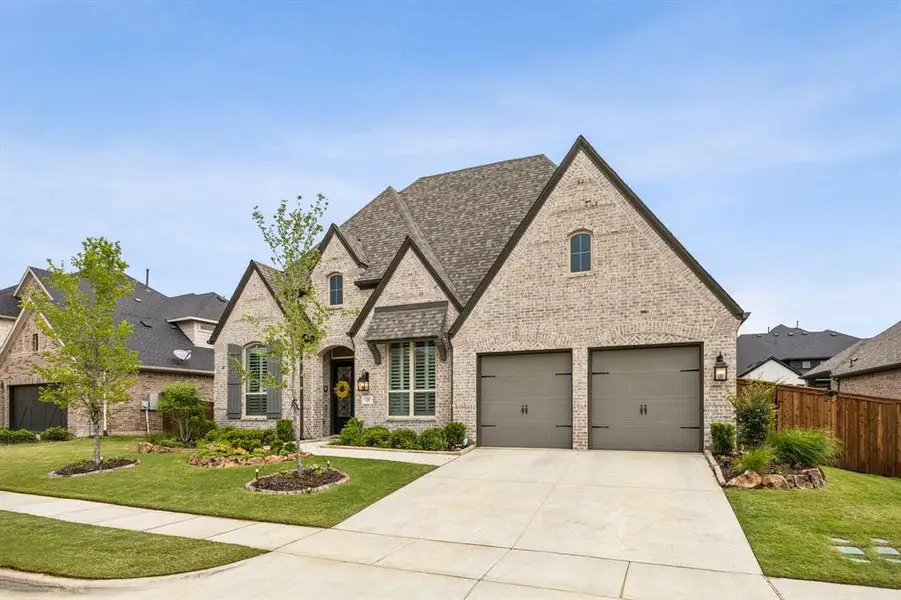 French provincial home with brick siding, concrete driveway, and roof with shingles
