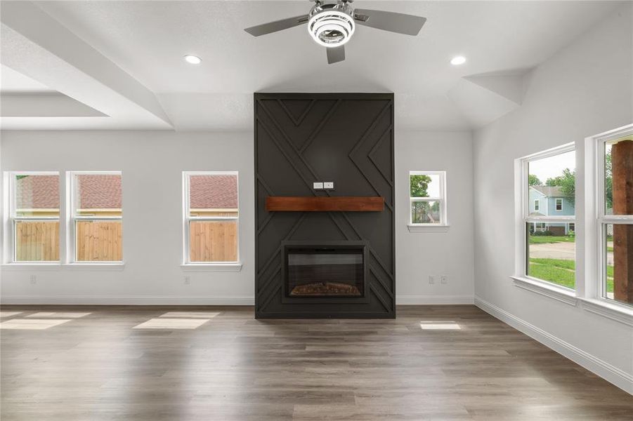 Living area featuring a floor-to-ceiling fireplace with an electric insert and wood mantel, vaulted ceilings with recessed lighting, a ceiling fan with integrated lighting, and wood-finish flooring