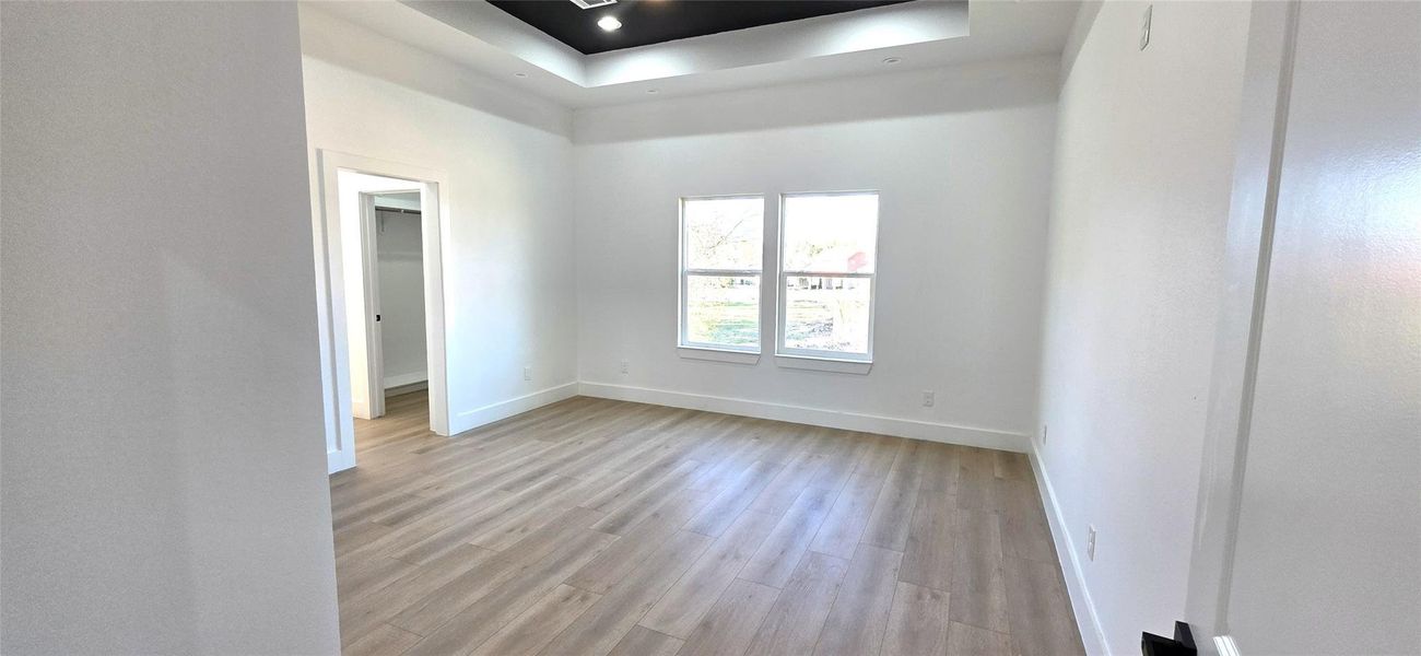 Experience tranquility in this bright primary bedroom, featuring elegant tray ceilings, ample natural light, and sleek hardwood floors.