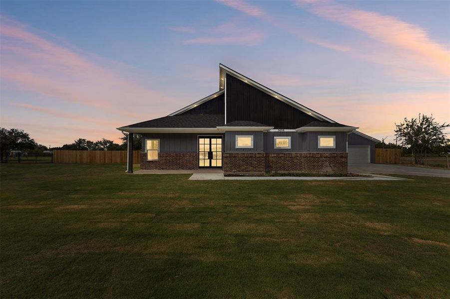 Front of property at dusk featuring a garage, concrete driveway, brick siding, and board and batten siding