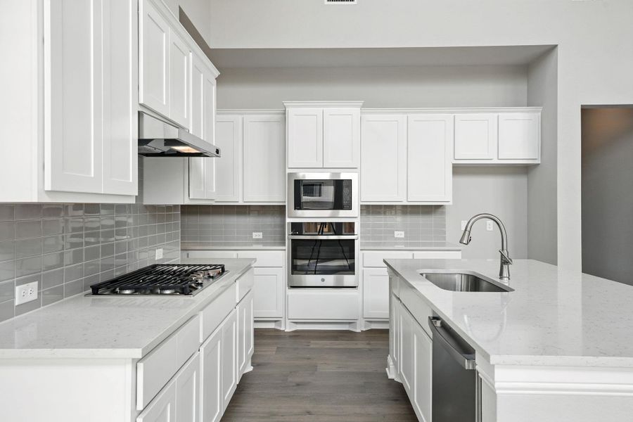 Kitchen with a center island with sink, light stone counters, stainless steel appliances, and white cabinets Kitchen with a center island with sink, light stone counters, stainless steel appliances, and white cabinets