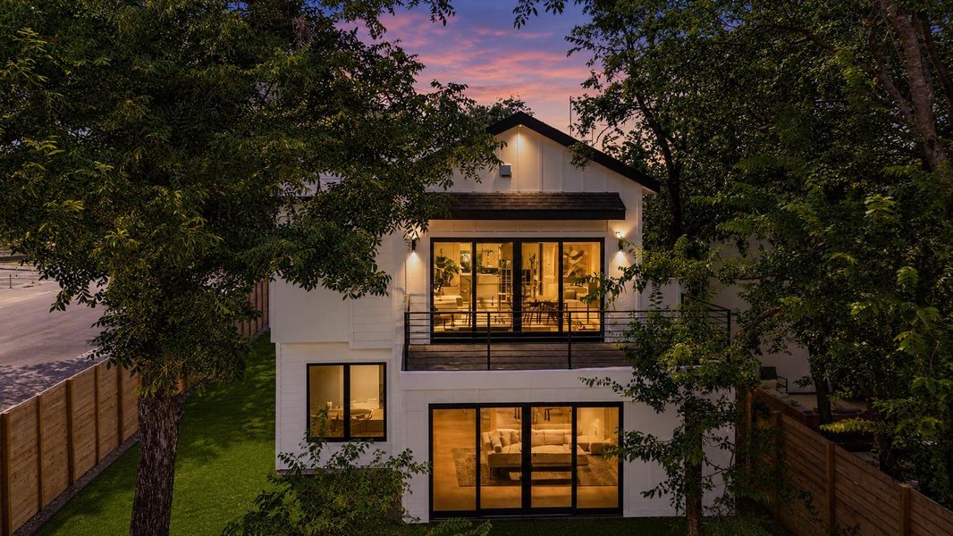 Dramatic sunset hues embrace this modern home, featuring multiple glass doors that open to an outdoor deck.