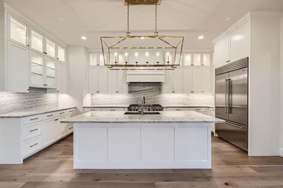 Kitchen with light hardwood / wood-style flooring, stainless steel built in fridge, light stone counters, and a large kitchen island with sink