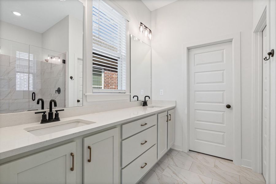 Bathroom featuring double vanity, light marble finish flooring, and a shower stall