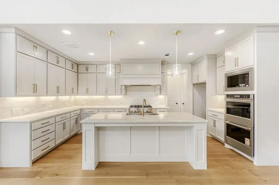 Kitchen with a kitchen island with sink, stainless steel appliances, light wood-style floors, and hanging light fixtures