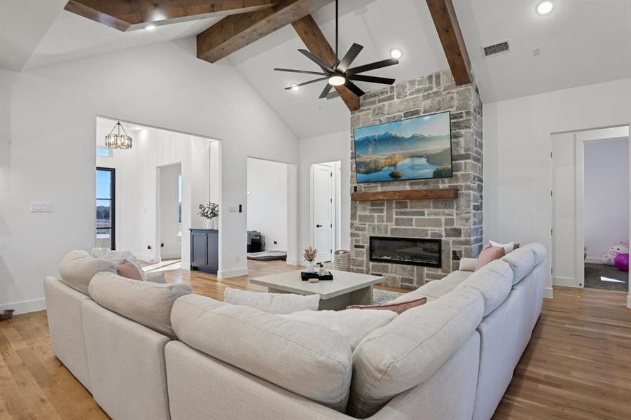 Living room with a stone fireplace, high vaulted ceiling, ceiling fan, light wood-type flooring, and beam ceiling Living room with a stone fireplace, high vaulted ceiling, ceiling fan, light wood-type flooring, and beam ceiling