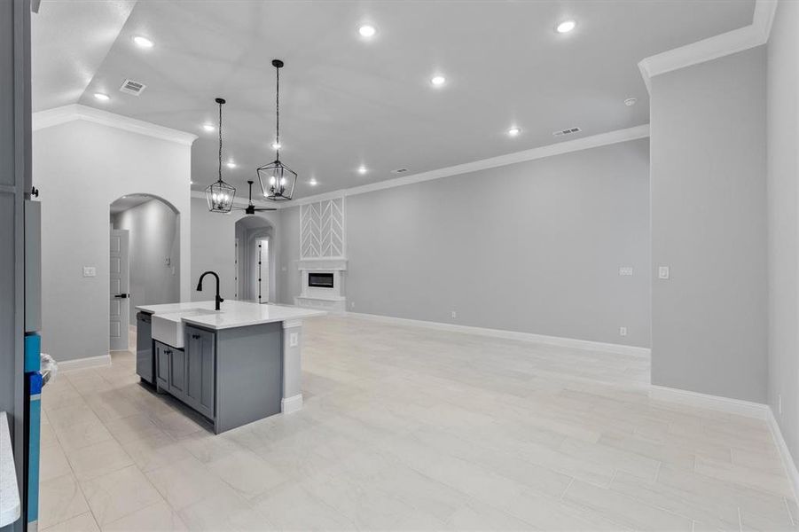 Kitchen featuring a center island with sink, sink, gray cabinets, crown molding, and decorative light fixtures