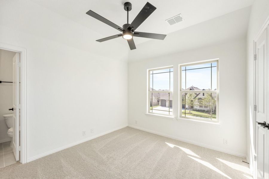 Empty bedroom with carpet, ceiling fan, two windows, and ensuite bathroom door visible