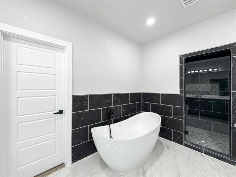 Full bathroom featuring tile walls, a shower stall, a freestanding tub, a wainscoted wall, and marble finish flooring