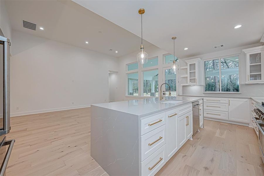 open-concept with a large island, white cabinetry, gold accents, and pendant lighting.