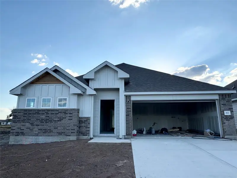 View of front of property with board and batten siding, driveway, an attached garage, and roof with shingles