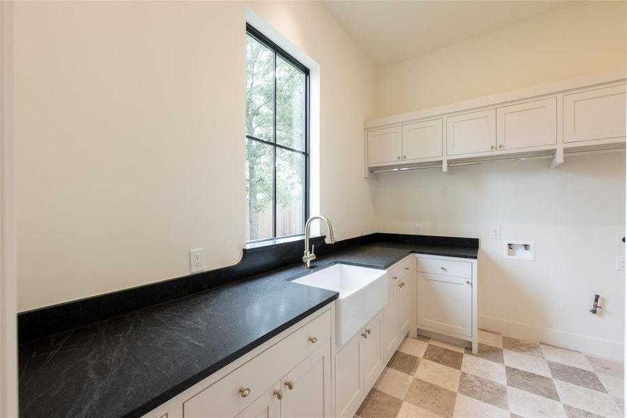 Connected directly to the primary closet, this laundry room features honed soapstone counters, a farmhouse sink, and checkered stone flooring. Ample cabinetry and natural light make the space both functional and inviting. Connected directly to the primary closet, this laundry room features honed soapstone counters, a farmhouse sink, and checkered stone flooring. Ample cabinetry and natural light make the space both functional and inviting.