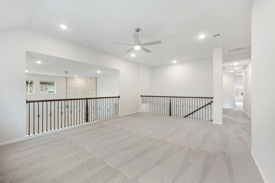 Open upstairs loft with carpet flooring, ceiling fan, and wrought iron stair railings overlooking lower level Open upstairs loft with carpet flooring, ceiling fan, and wrought iron stair railings overlooking lower level