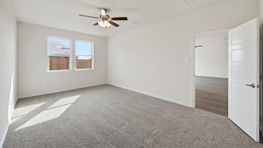 Spacious room featuring neutral carpeting, a ceiling fan with integrated lighting, and two windows providing natural illumination Spacious room featuring neutral carpeting, a ceiling fan with integrated lighting, and two windows providing natural illumination