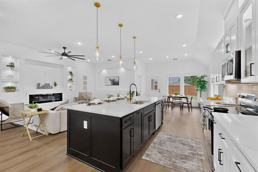 Open-concept living space featuring wood-finish flooring, a contemporary kitchen island with a built-in sink, white shaker-style cabinetry with black hardware, and a modern linear fireplace with built-in shelving