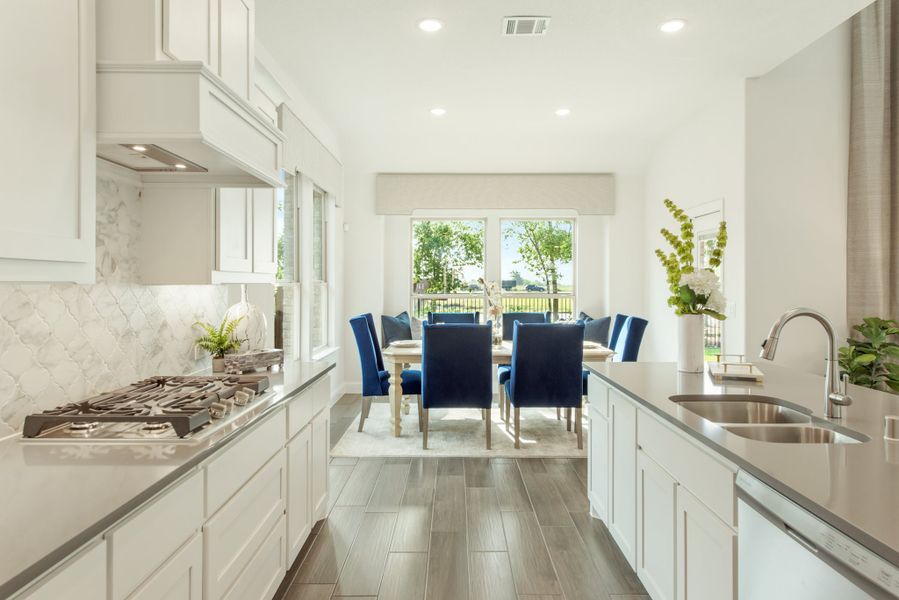 Open kitchen with white cabinets, gas cooktop, and dining area with blue chairs visible beyond the island.
