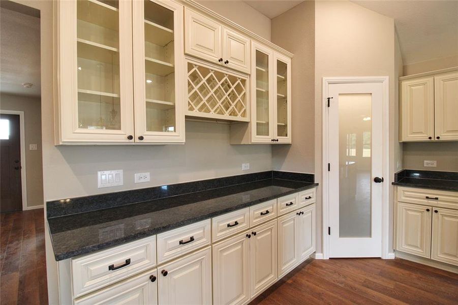 Kitchen featuring dark wood-type flooring, dark stone counters, glass insert cabinets, and cream cabinets