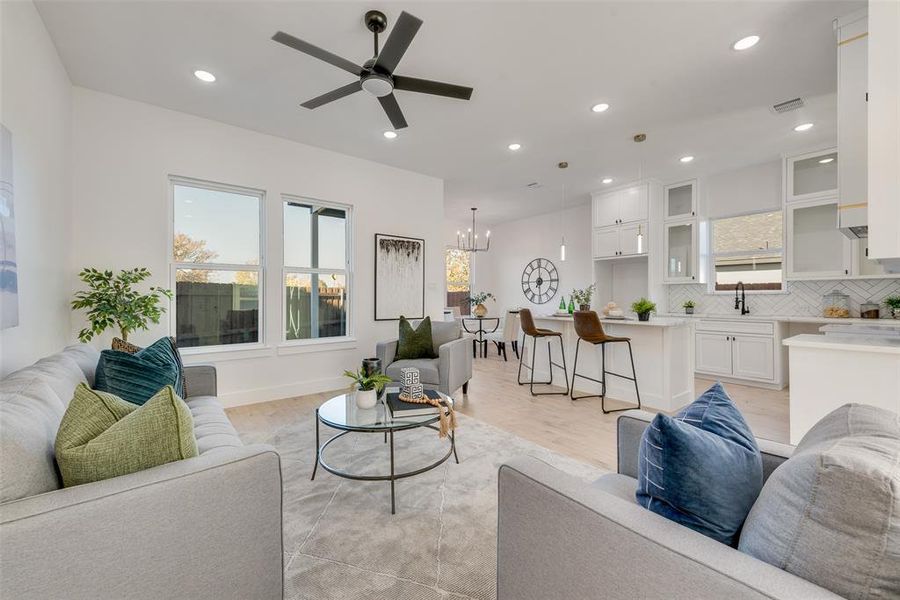 Living room with ceiling fan with notable chandelier, light wood-type flooring, and sink