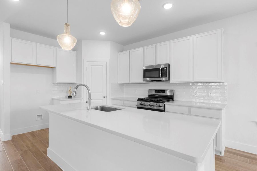 Bright and modern gourmet kitchen featuring sleek quartz countertops, white shaker cabinets, beautiful crisp white tile subway backsplash, deep undermount stainless steel sink with swan pull out kitchen faucet.