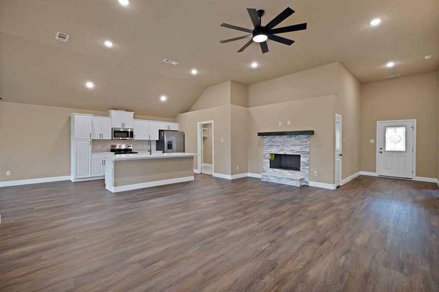Unfurnished living room featuring vaulted ceiling, a ceiling fan, a stone fireplace, dark wood-style flooring, and visible vents Unfurnished living room featuring vaulted ceiling, a ceiling fan, a stone fireplace, dark wood-style flooring, and visible vents