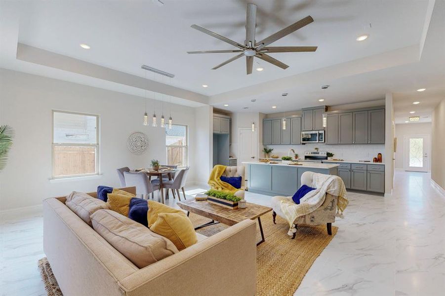 Living room featuring ceiling fan, a tray ceiling, and light tile flooring