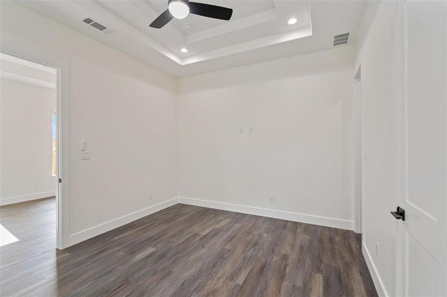 Empty room with a ceiling fan, dark wood-style floors, recessed lighting, and a raised ceiling