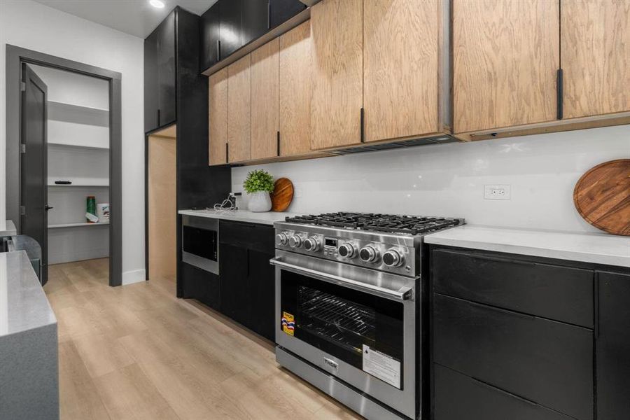 Kitchen with stainless steel appliances, light wood-type flooring, light stone counters, and dark cabinetry