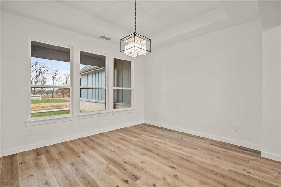 Unfurnished dining area with a tray ceiling, a notable chandelier, and light hardwood / wood-style flooring