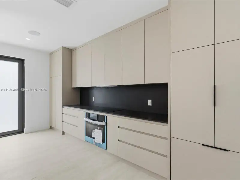 Kitchen featuring minimalist floor-to-ceiling cabinetry, matte black hardware, solid-surface countertops, contrast backsplash, and integrated oven Kitchen featuring minimalist floor-to-ceiling cabinetry, matte black hardware, solid-surface countertops, contrast backsplash, and integrated oven